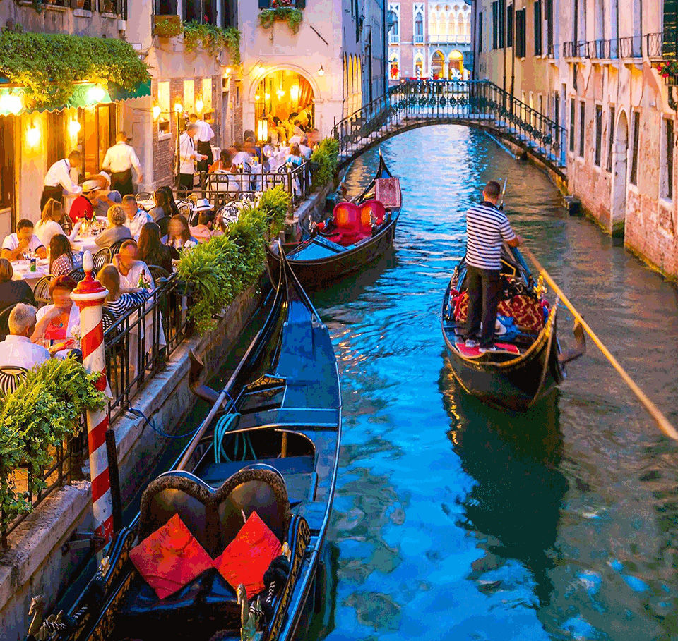 People dining along a canal in Venice as a gondola passes.