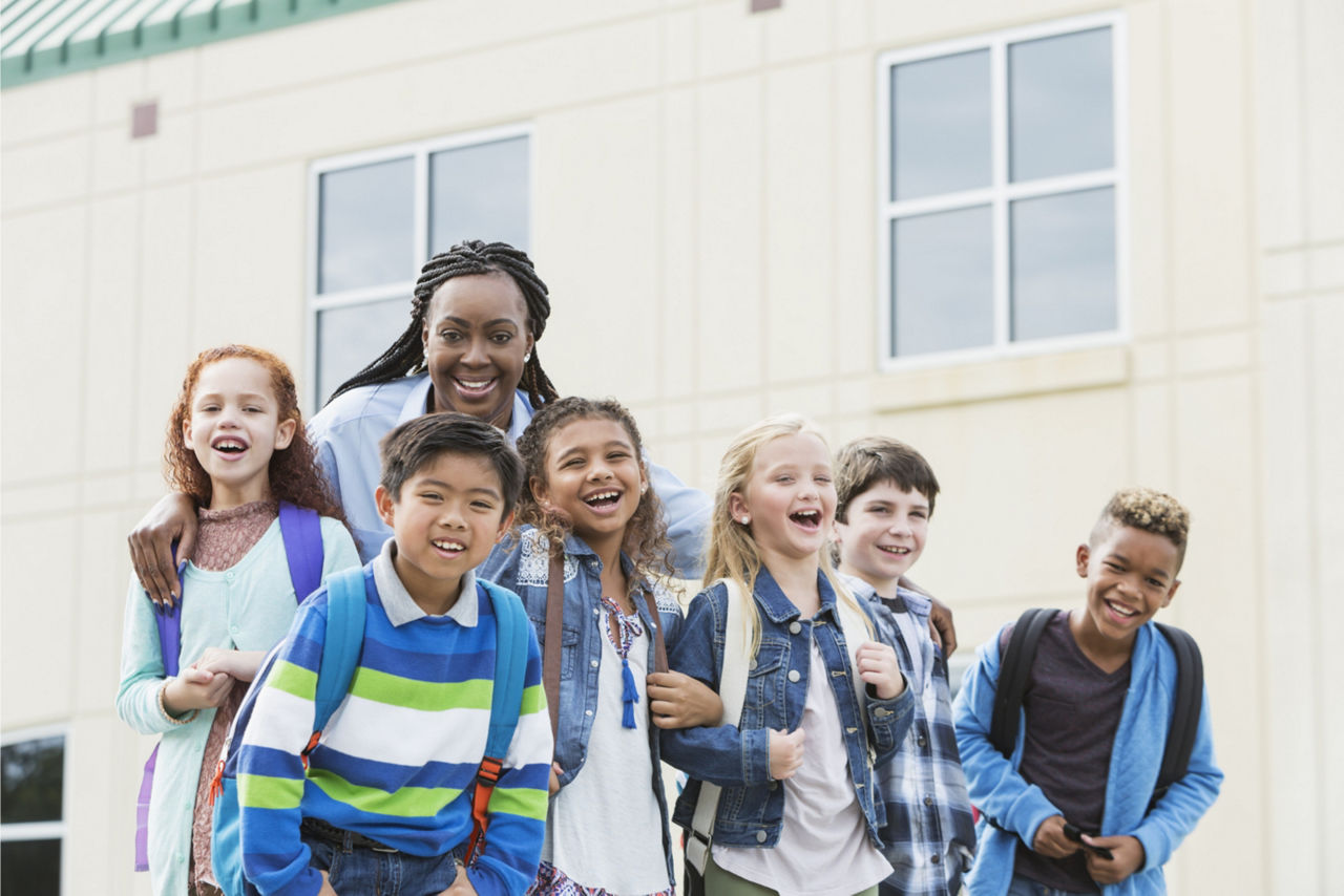 Teacher stands outside the school building taking a picture with her students. 
