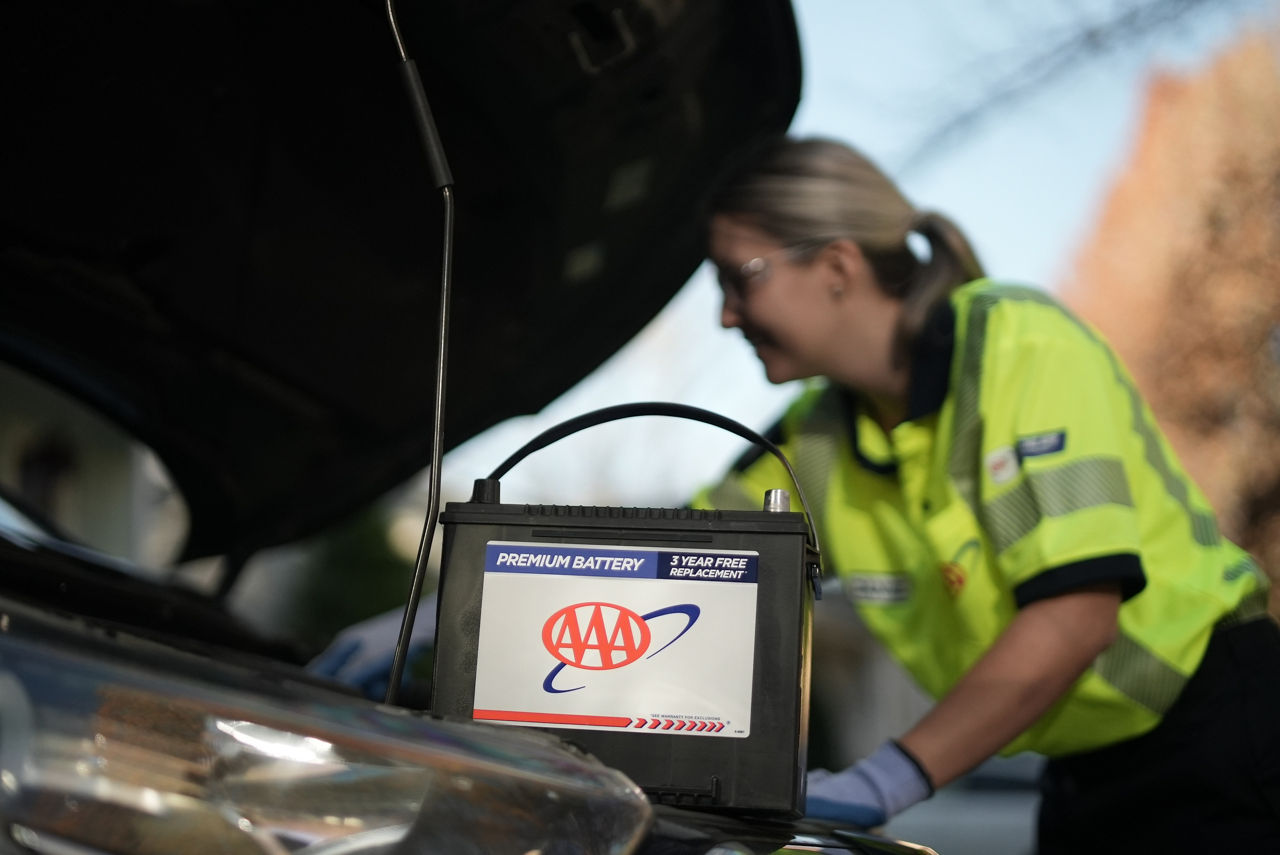 AAA technician under the hood of a car, installing a AAA vehicle battery.