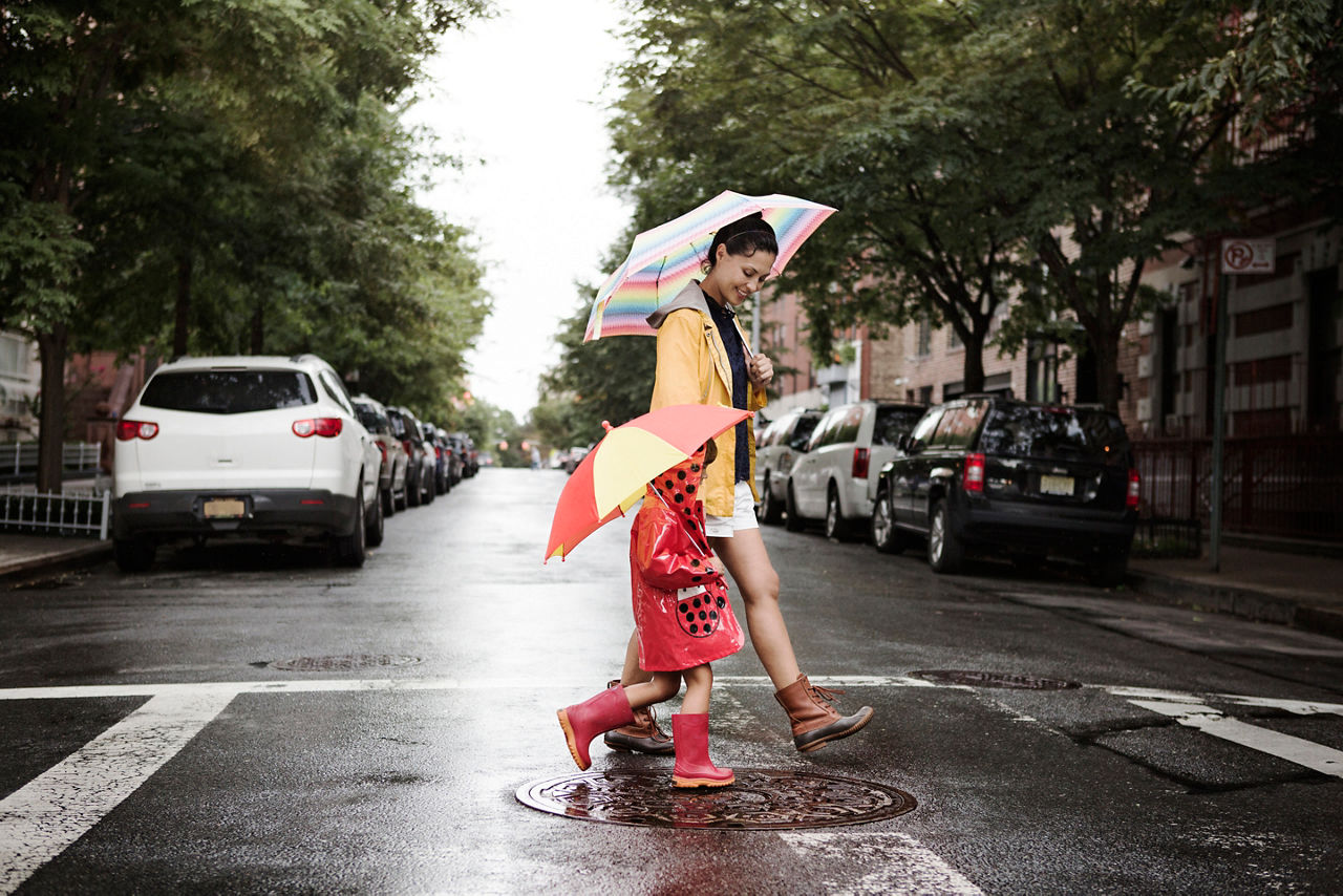 Side view of mother and daughter holding umbrellas while crossing road 
