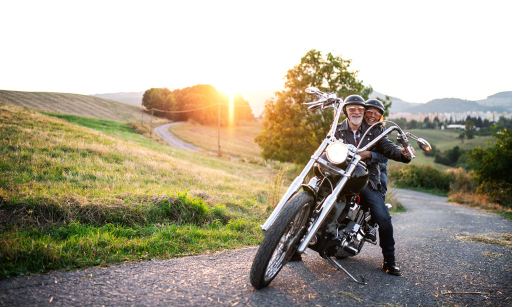 A cheerful senior couple travelers with motorbike in countryside. 