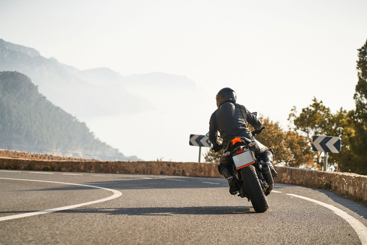 Back shot of man riding sport motorbike taking a curve surrounded by nature at mountain