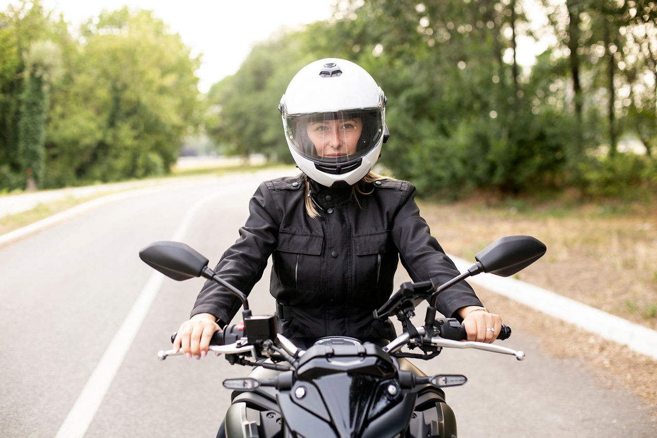 Young woman riding a motorcycle on a road. About 25 years old, Caucasian female.