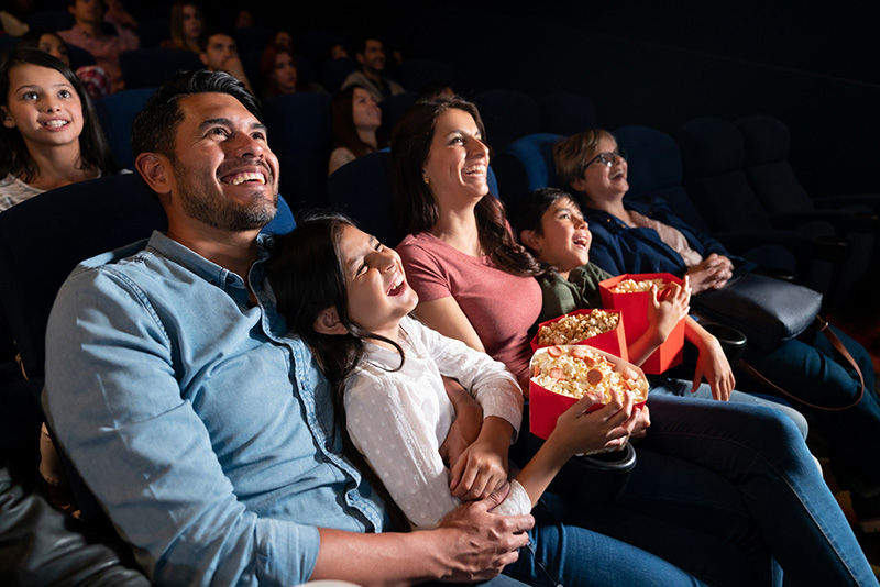 Happy Latin American family watching a comedy film at the cinema and laughing - entertainment concepts