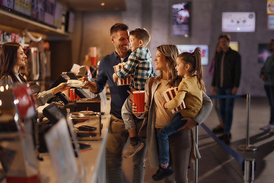 Happy parents and their kids buying movie tickets at concession stand in cinema.