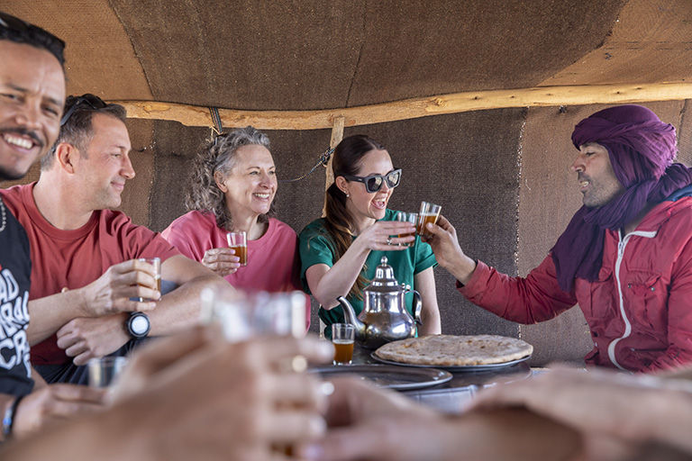 Travelers sharing tea and conversation under desert tent canopy