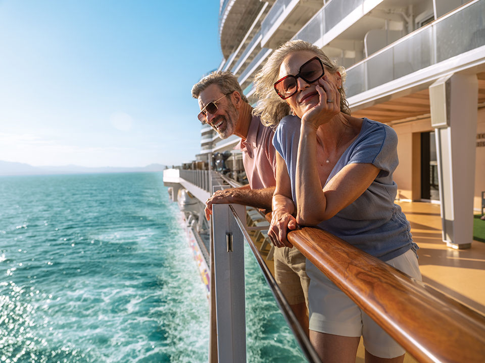 Happy, mature couple on the railing of Norwegian Aqua cruise ship sailing at sea.