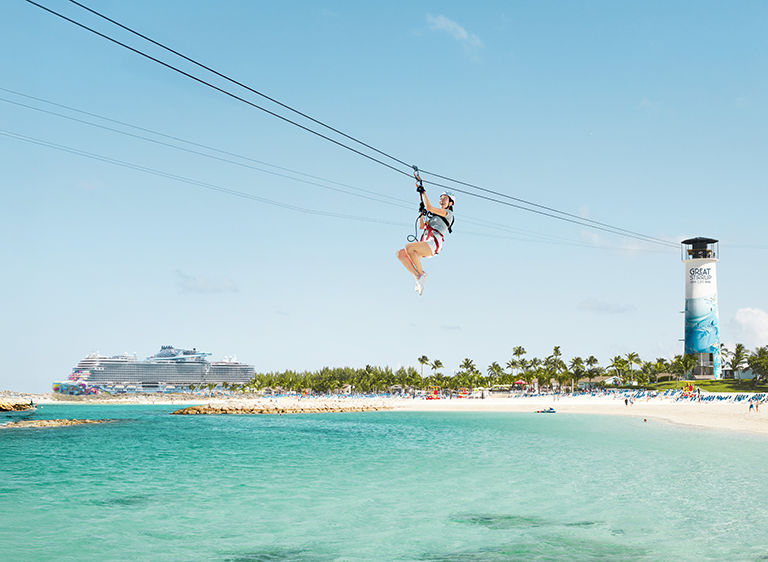 Norwegian crusie ship in the background with a woman on a zip line at Graet Stirrup Cay.