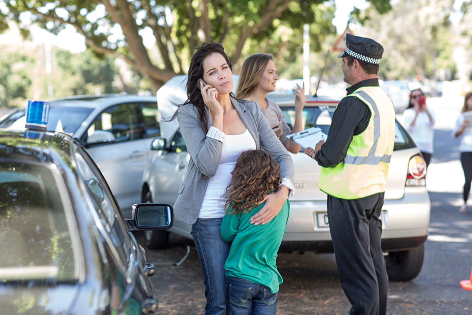 Mom holds her child why she is at the scene of a car incident filing her insurance claim and getting assistance from aaa.