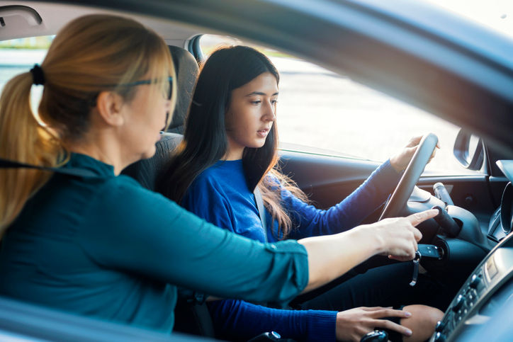 A teenage girl sitting behind the steering wheel of a car and listening to her mothers instructions as she drives.
