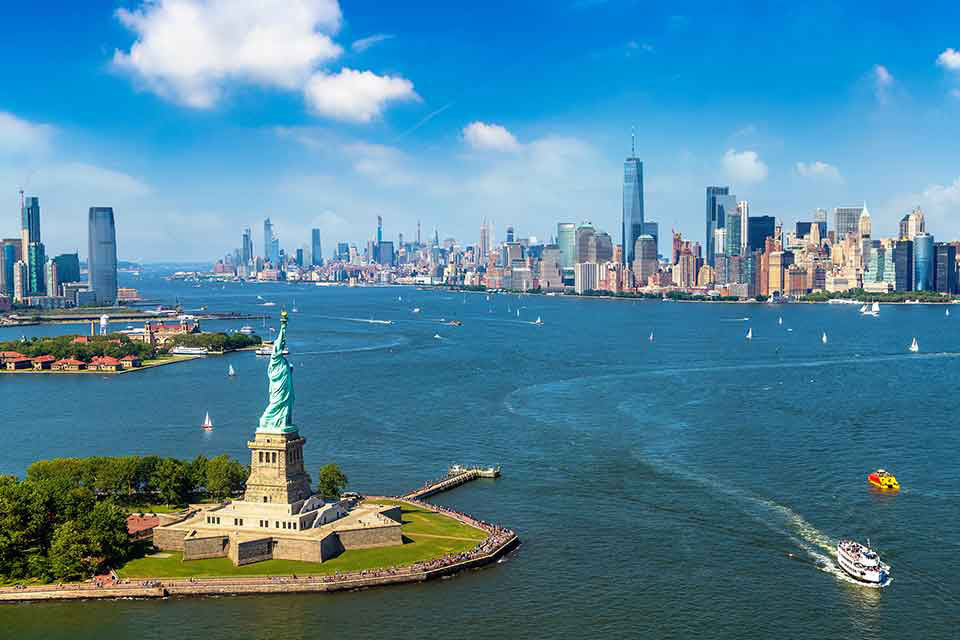 Statue of liberty looks out to the new york skyscrapers with boats driving by.