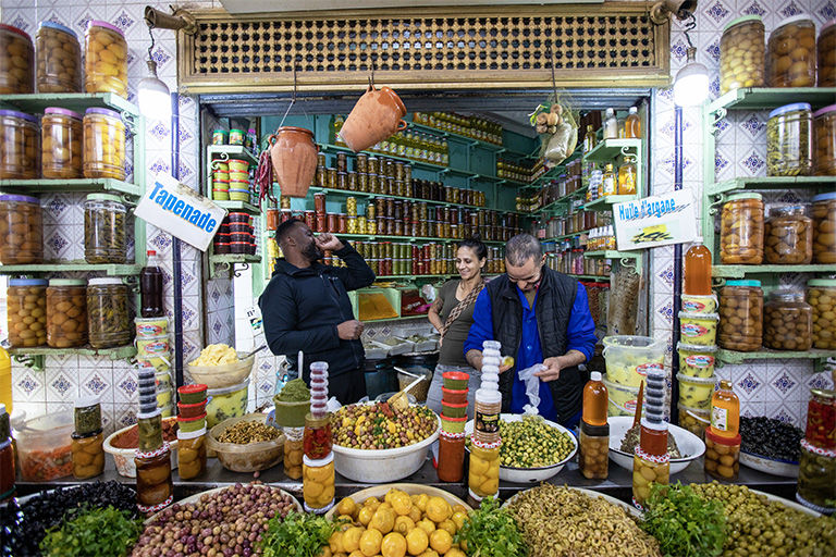 Immersive market experience with pyramids of olives, spices, and traditional preserved goods.