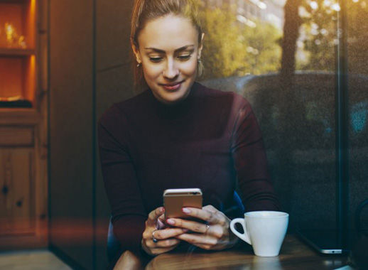 Woman handling her AAA banking accounts on her smartphone while at a coffee shop.
