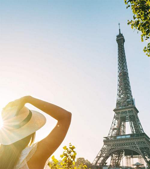 A girl holding her hat as she looks up at the Eiffel Tower in Paris, France