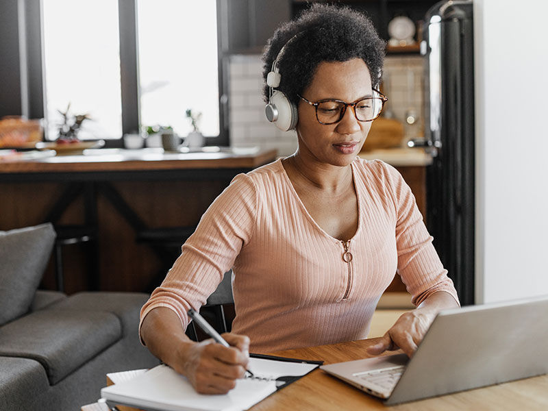A women sits at her desk with her headphones on listening to a AAA webcast while taking notes. 