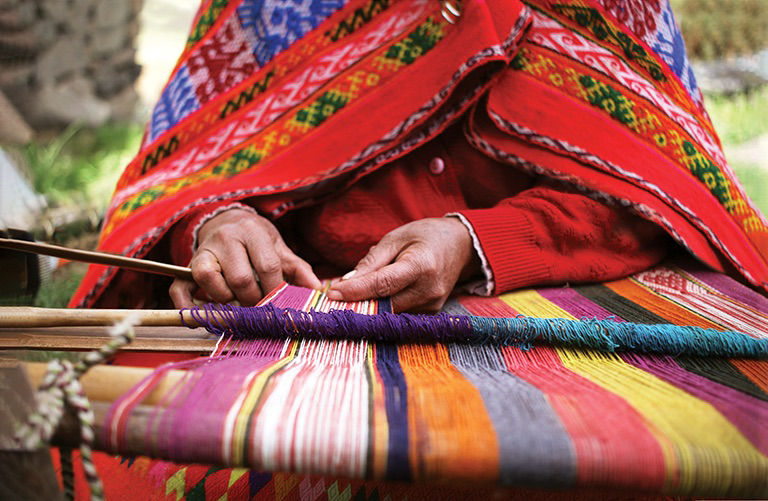 A close up of a woman weaving in Peru with bright traditional clothes.