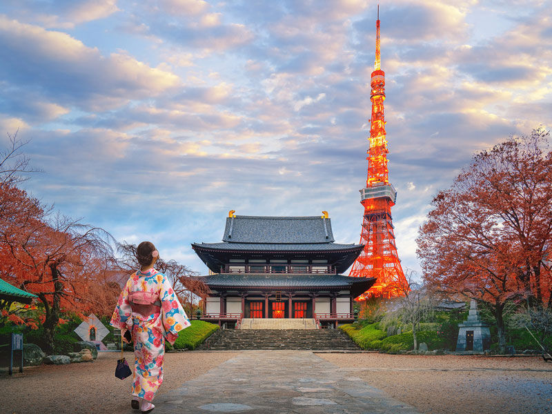 A scene in Japan with a woman in a traditional kimono walking toward a Japanese shrine