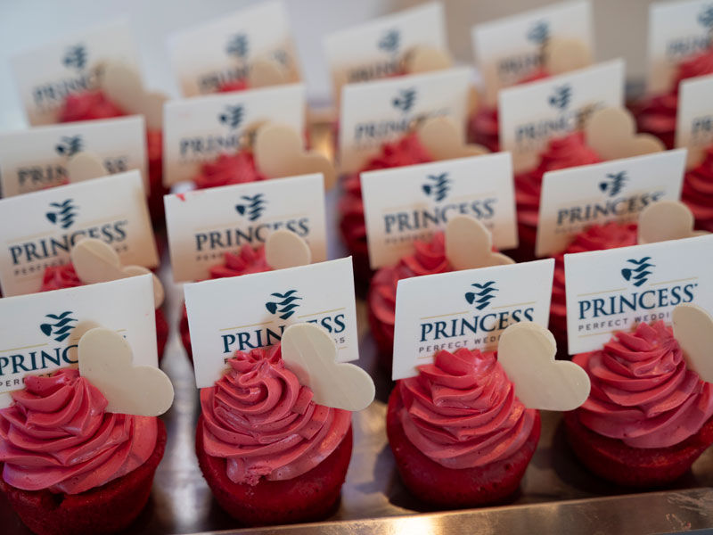 A row of pink cupcakes with Princess Cruises welcome cards