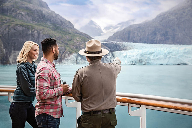 Couple on cruise ship in Alaska with a park ranger at the railing looking at wildlife.
