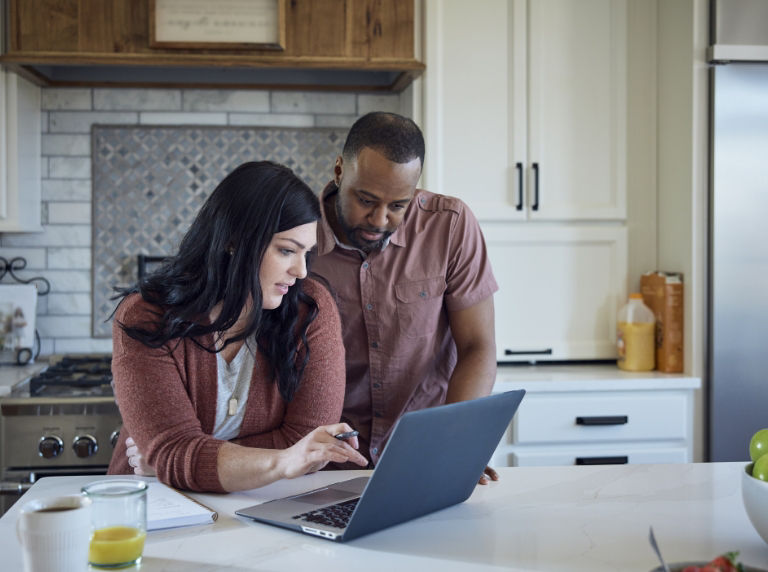 black and white couple in kitchen looking at a laptop