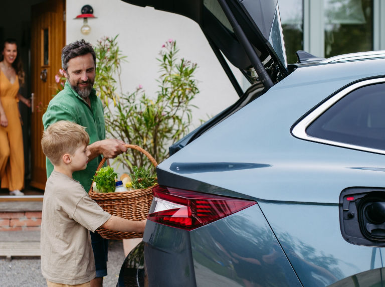 A man with his son grabbing a basket full of groceries out of the trunk of the car.