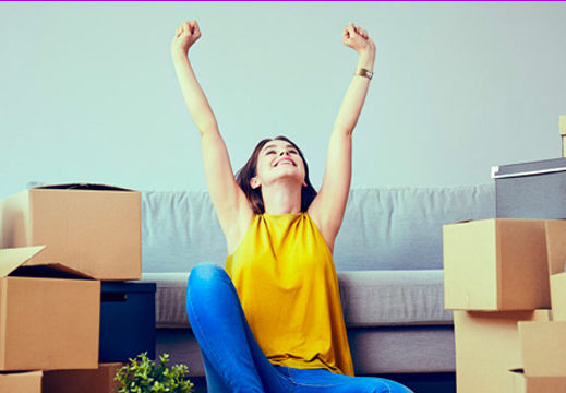 Young adult surrounded by moving boxes in their new living room.
