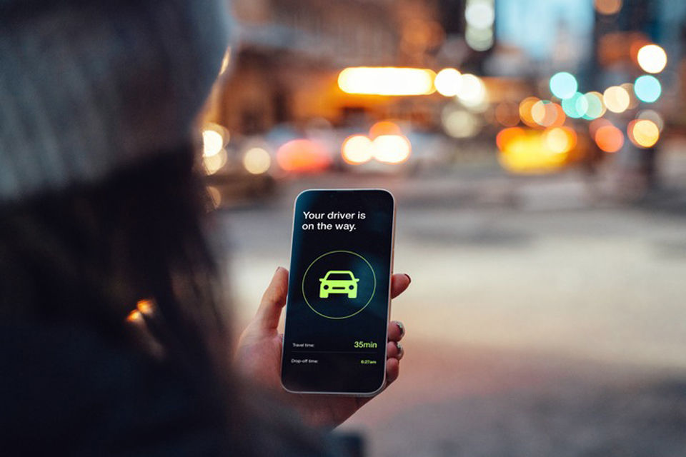 Over the shoulder view of young woman using mobile app on smart phone to arrange ride share service.