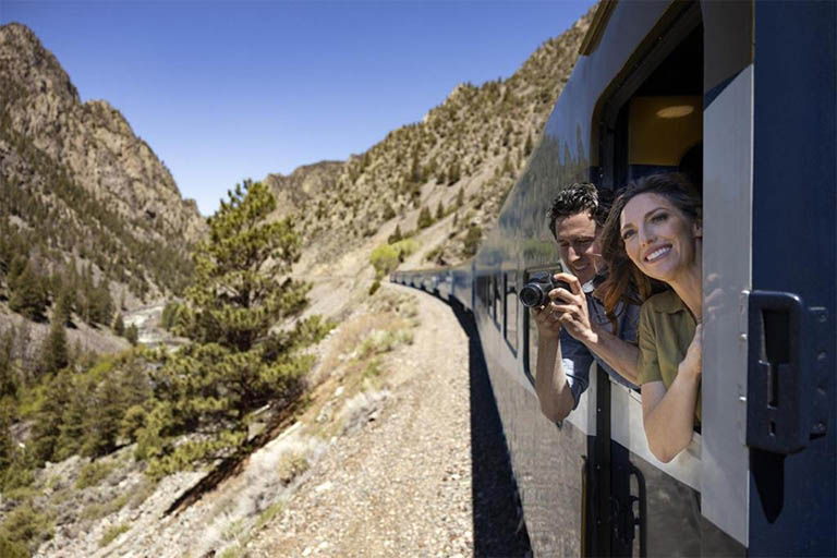 Couple looking out of a Rocky Mountaineer train and taking pictures.
