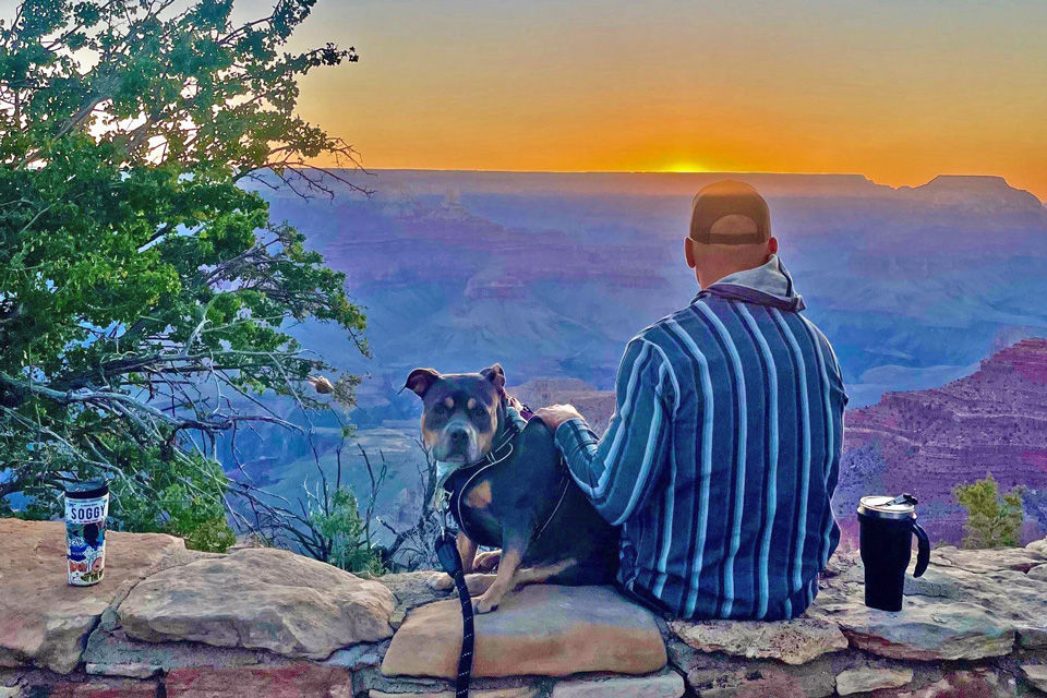 A man and his dog watch the sunset together during their road trip.