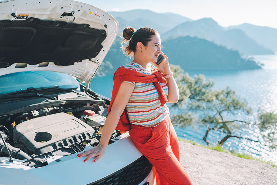Concentrated mature woman in orange outfit trying to fix her broken car, calling to roadside service online