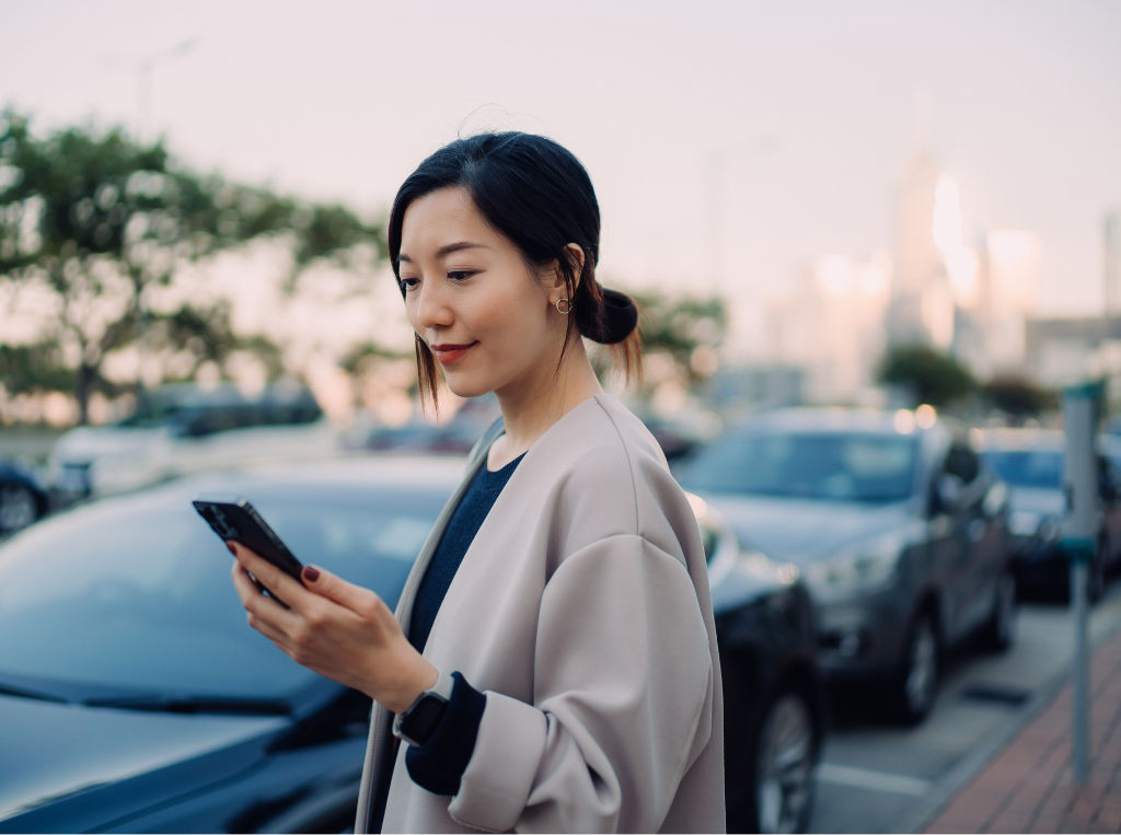 Woman looking at her cell phone by her car.