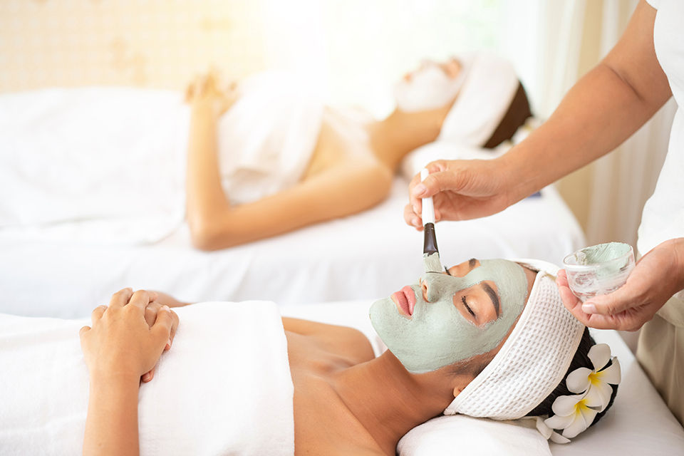 Beautician applying enzymatic peeling on woman's face in spa