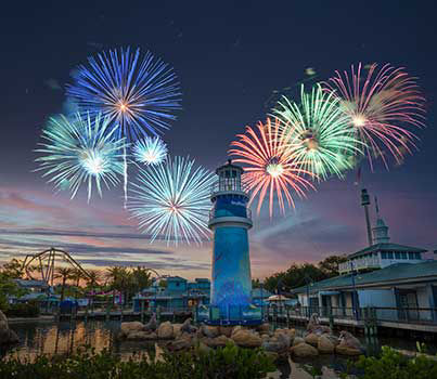 Seaworld's lighthouse in the foreground with sea lions lounging on rocks at night with fireworks going off in the background.