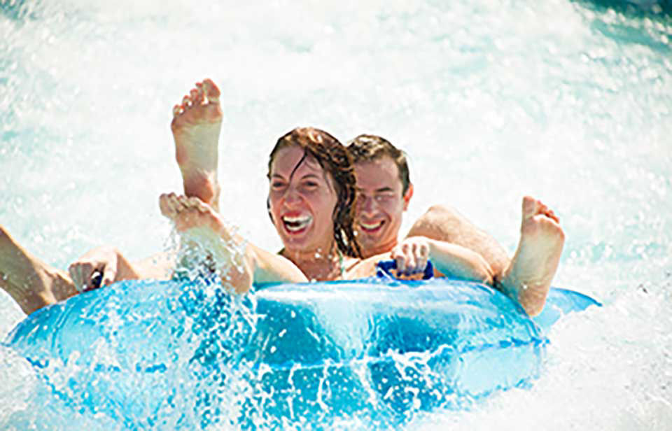 Couple is going down whanau way waterslide in aquatica park with water splashing all around them.