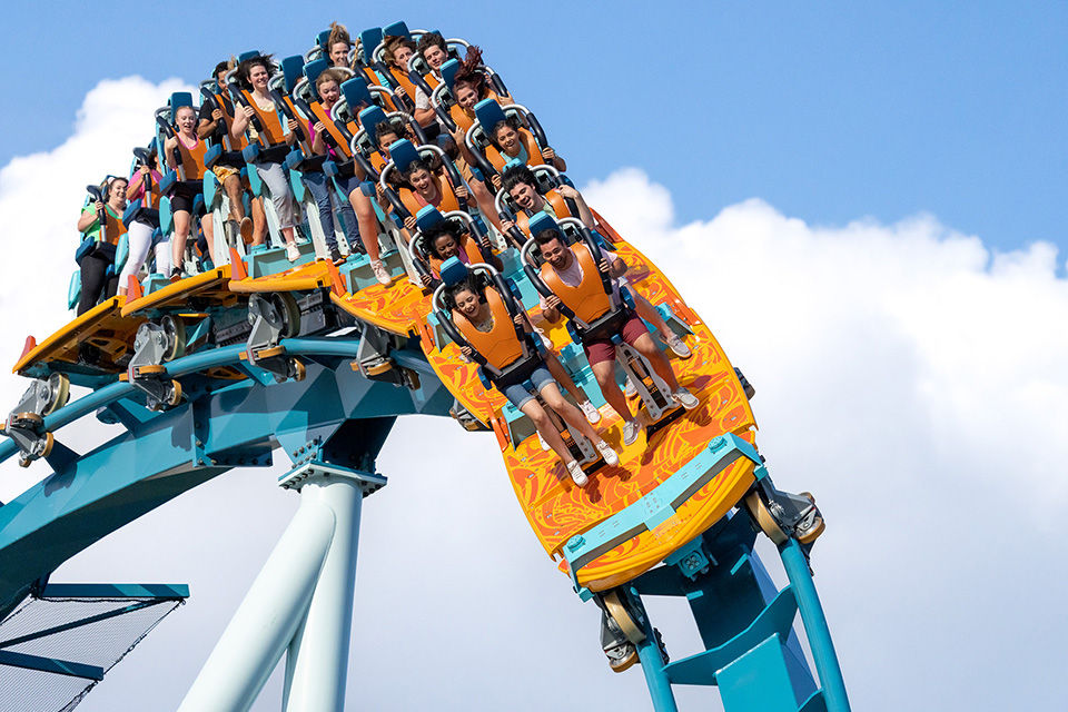 Group of people ride a bright orange and turquoise blue roller coaster.