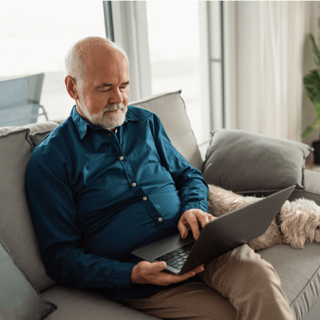 Senior man sitting on sofa with his dog and using laptop at home