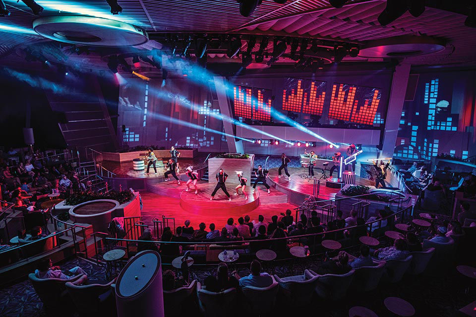 Ovation of the Seas, Two70 show, roboscreens, Pixels, entertainment, night, wide shot of performers on stage, singing, singers, actors, dancers, musicians playing, audience in round, spotlights.