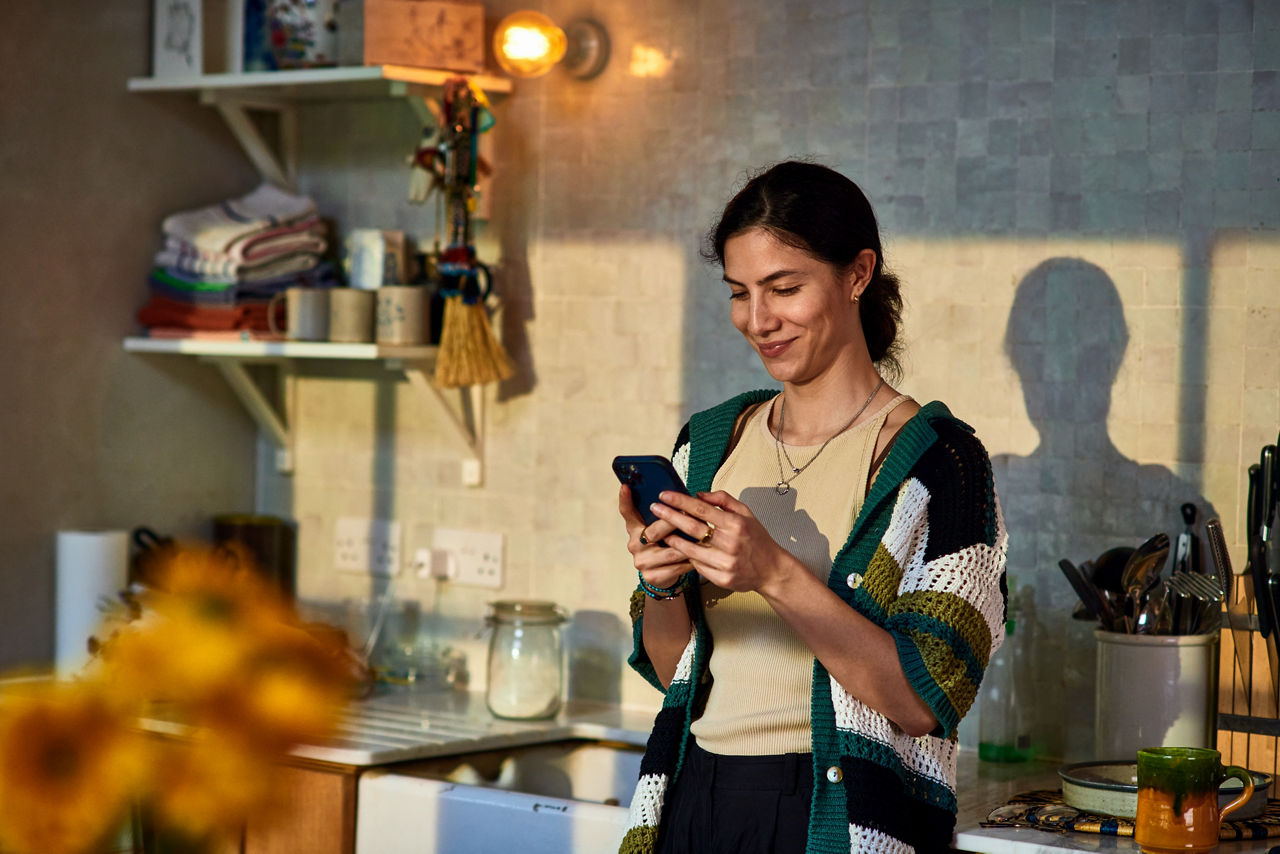 Smiling woman in her 30's standing in kitchen texting on smart phone, communication, wireless technology, the internet