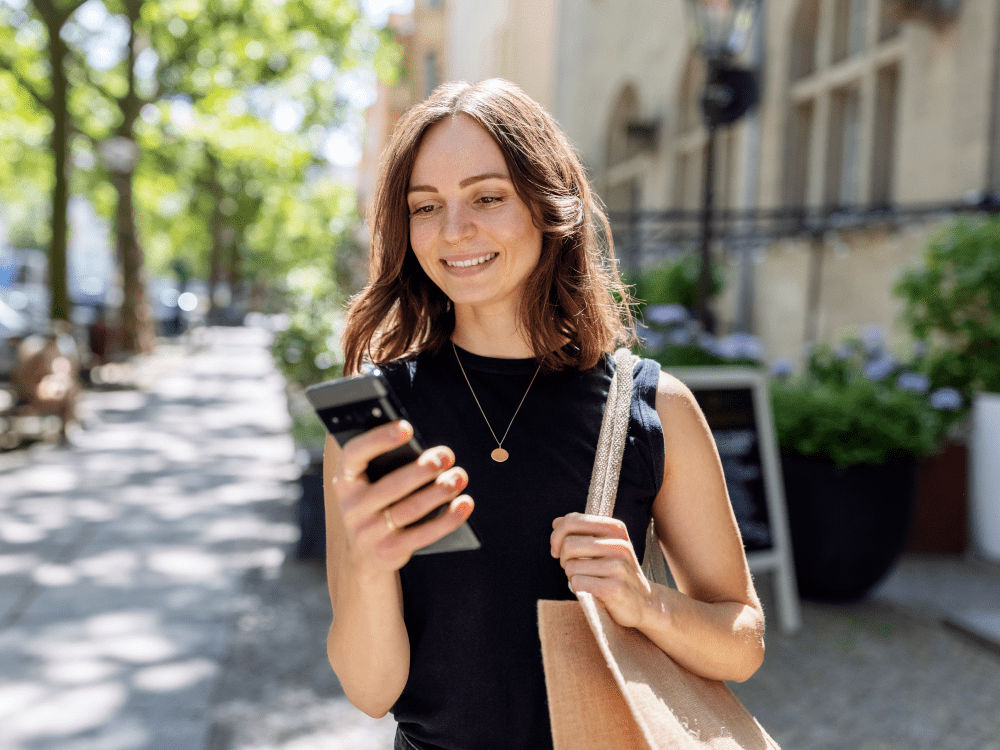 Smiling young woman walking outdoors and checking messages on her mobile phone. 