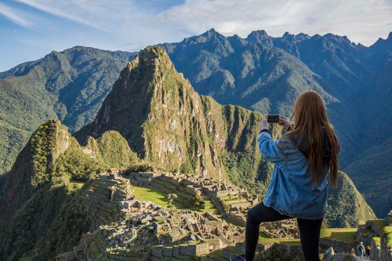 Solo traveler capturing the famous view of Incan ruins nestled between dramatic peaks.