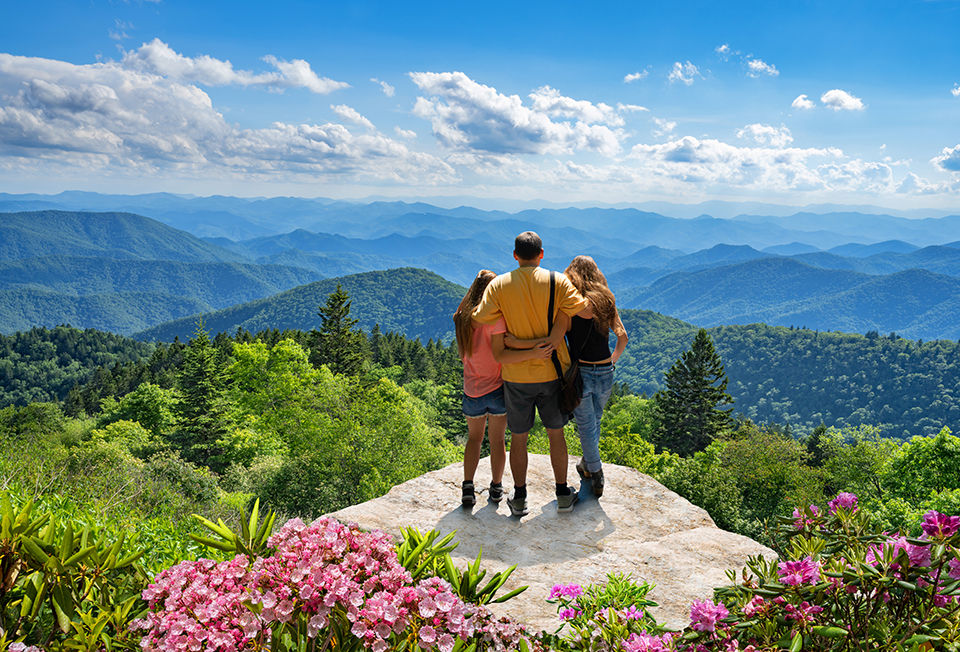 Family standing with arms around on top of the mountain, looking at beautiful summer mountains landscape. People hiking on vacation, enjoying beautiful view. North Carolina, USA.
