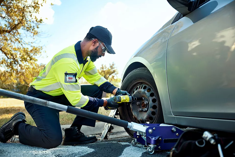 AAA roadside assistance technician replacing a flat tire.