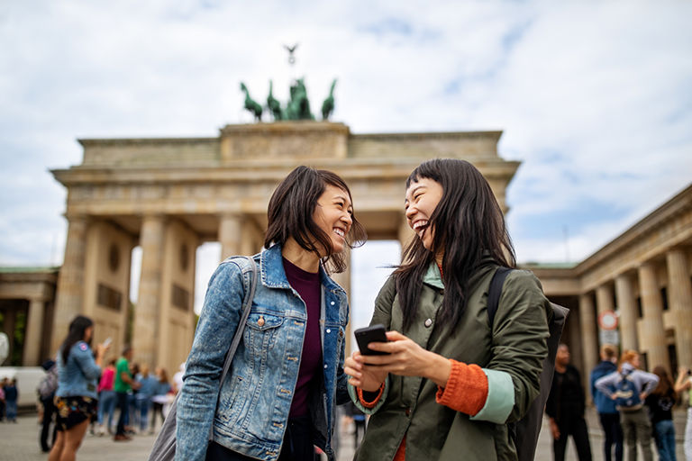 Cheerful female friends standing against Brandenburg Gate in city during vacation.