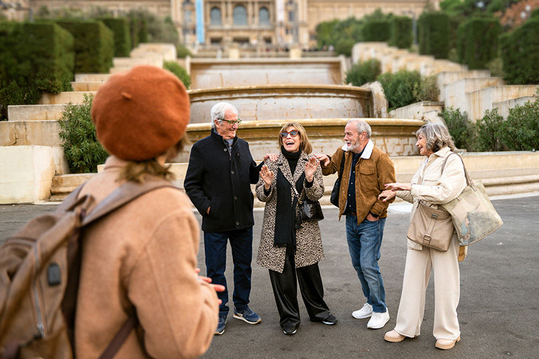 Two older couples standing in front of an old fountain at a palace.