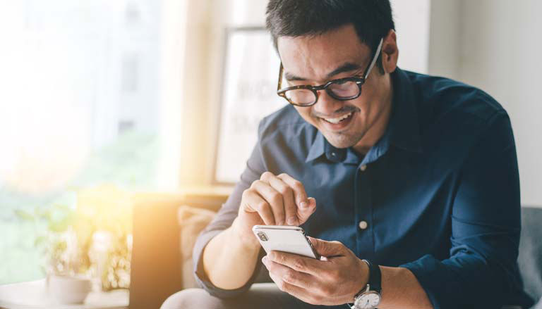 A man on a couch, booking travel with the AAA Mobile App.