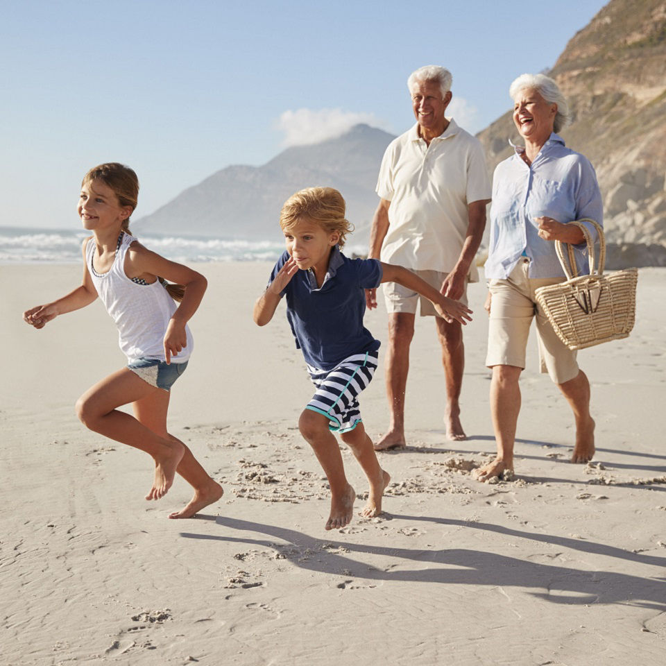 grandparents walking on beach with grandchildren running in front