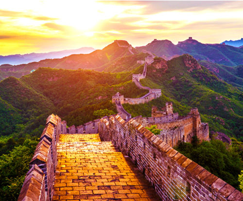 A panoramic view of the Great Wall of China along a set of green mountains.