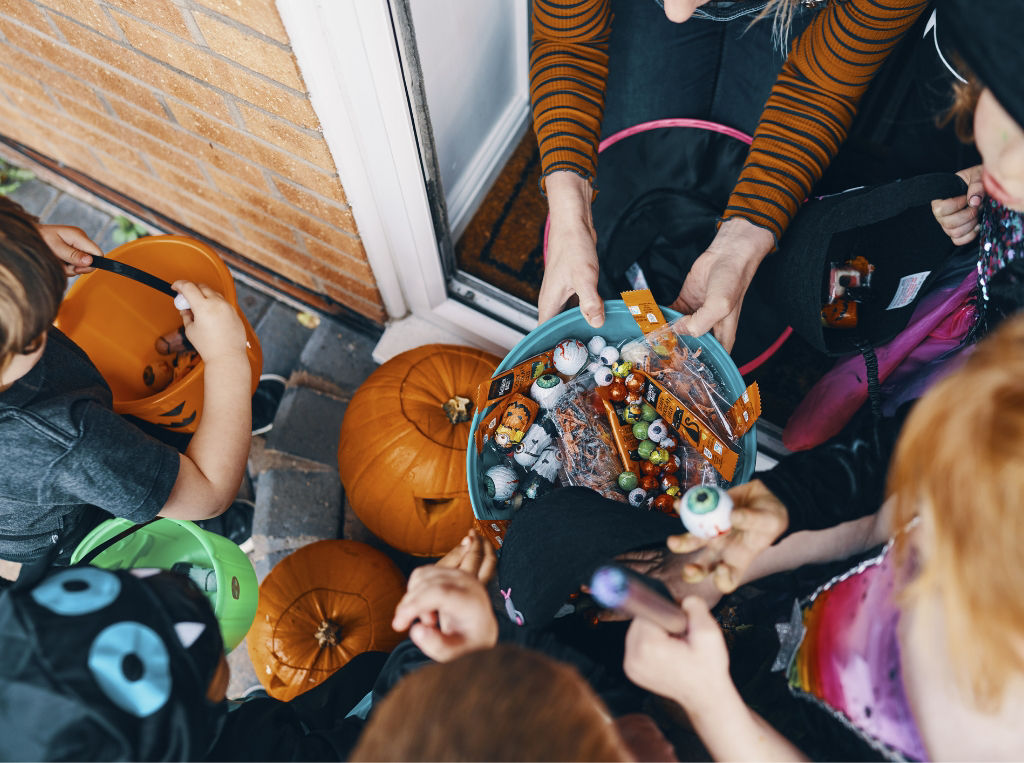 children taking candy from a bowl while trick or treating. 