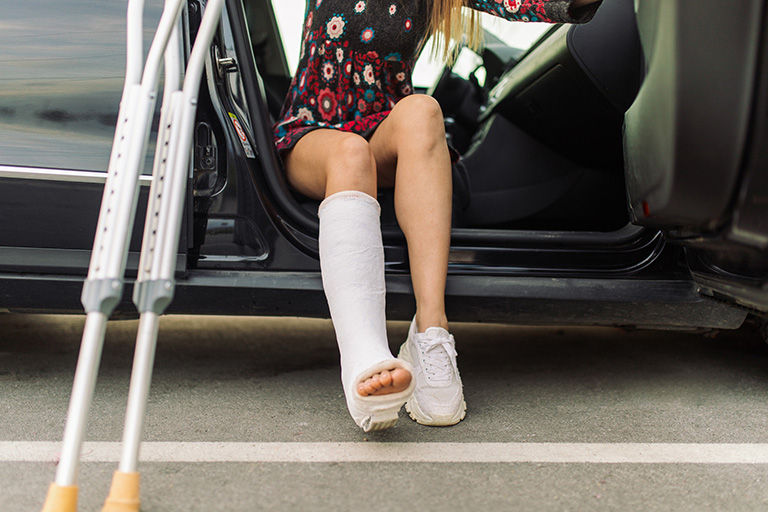 A mid adult woman with a cast on her leg in a beautiful floral long sleeved dress, getting out of car at parking lot downtown, holding a crutch