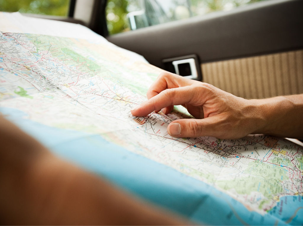 Passenger in a car using a printed map on their lap.